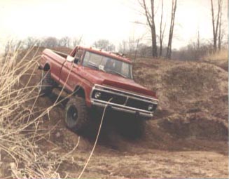 1979 Ford Bronco - This red pickup truck is navigating a steep, muddy incline with a tow rope connected to its front end.