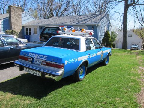 1991 Ford LTD Crown Victoria - A blue and white police car is parked on a grassy lawn in front of a house.