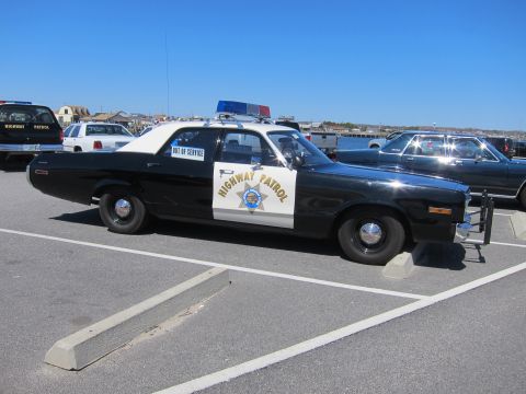1991 Ford LTD Crown Victoria - A vintage highway patrol car is parked in a lot with other vehicles under a clear blue sky.
