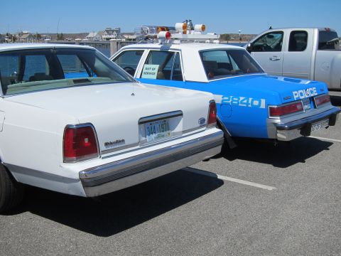 1991 Ford LTD Crown Victoria - Two police vehicles, a white 1991 Ford Crown Victoria LTD and a blue patrol car, are parked side-by-side.