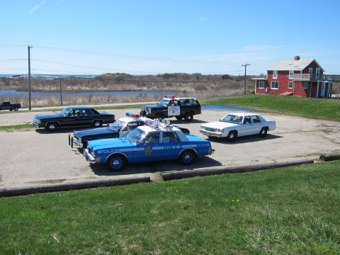 1991 Ford LTD Crown Victoria - A collection of police vehicles, including a blue and white sedan, a black SUV, and a white sedan, are parked in an outdoor lot.