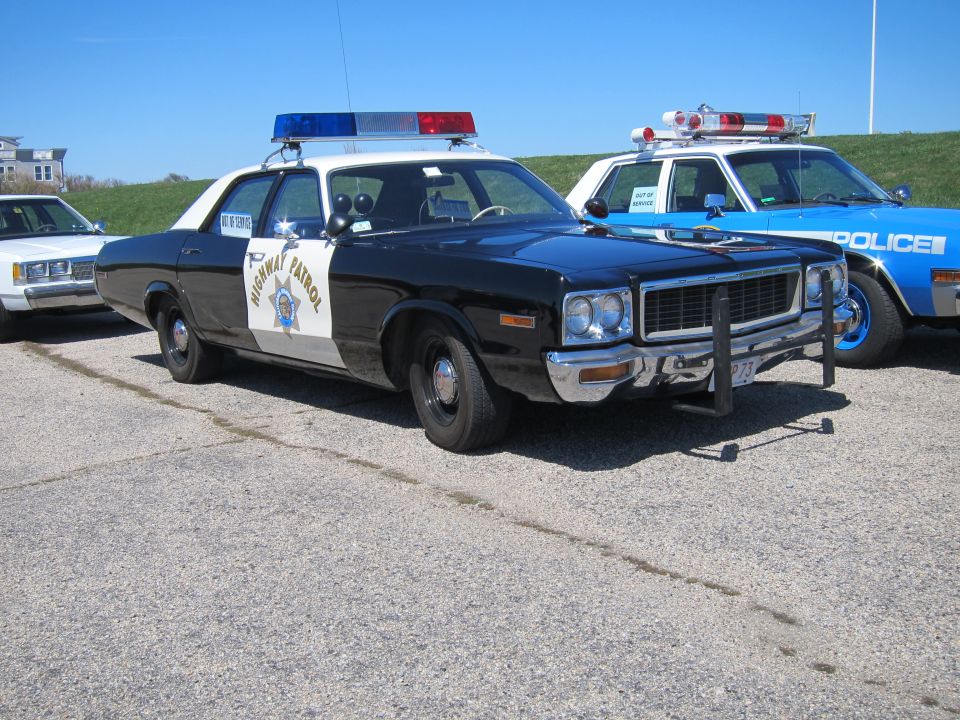 Black and white police car with "HIGHWAY PATROL" on the door, parked next to a blue police car