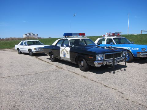 1991 Ford LTD Crown Victoria - Multiple police vehicles are lined up on a paved surface under a clear blue sky.