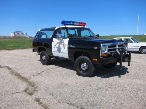 1991 Ford LTD Crown Victoria - A Dodge Ramcharger SUV, marked as Highway Patrol, is parked on a lot under a clear blue sky.