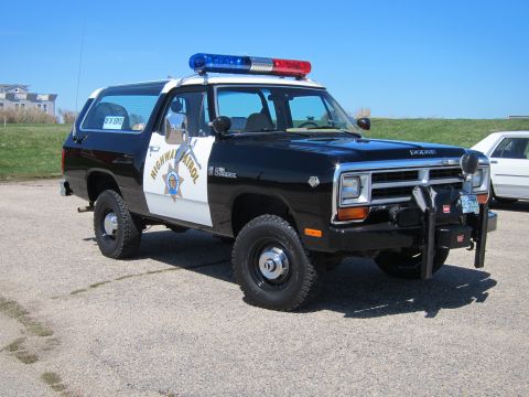 1991 Ford LTD Crown Victoria - A Dodge Ramcharger SUV, marked as Highway Patrol, sits parked on pavement under a clear blue sky.