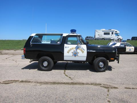 1991 Ford LTD Crown Victoria - A black and white highway patrol SUV is parked on asphalt, with another patrol car and an RV visible in the background.
