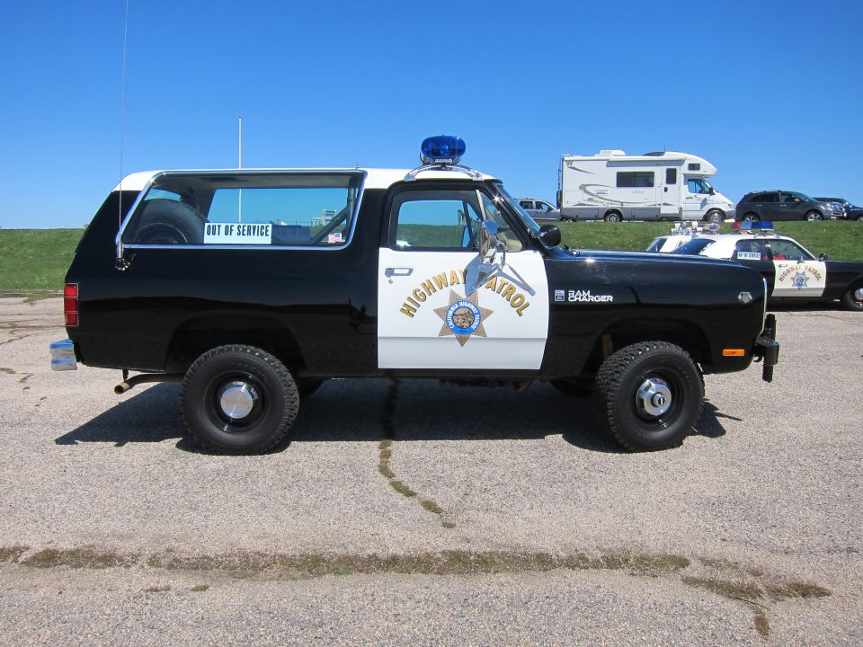 Black and white Dodge Ramcharger police SUV with "HIGHWAY PATROL" text and blue light bar. Another police car is visible behind it