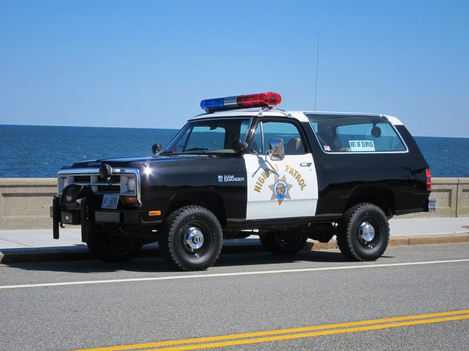 Black and white Dodge Ramcharger police SUV with light bar, parked by the ocean