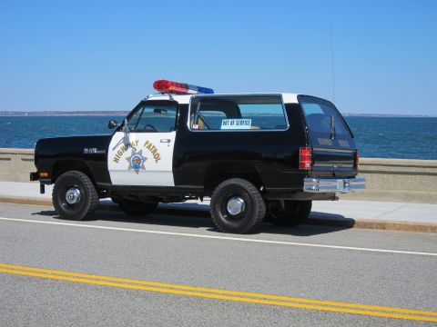 1991 Ford LTD Crown Victoria - This Dodge Ramcharger police SUV is parked near the water with a clear blue sky overhead.