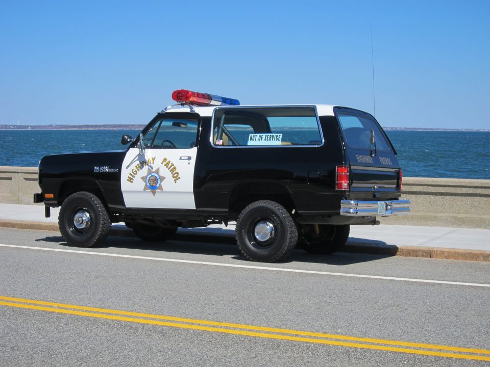 Black and white Dodge Ramcharger police SUV parked by the ocean, has a light bar on top and 'HIGHWAY PATROL' on the door