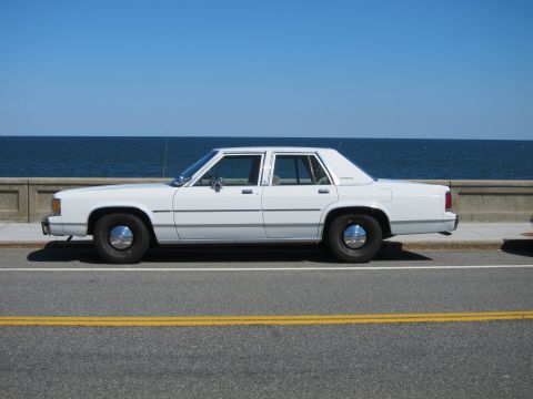1991 Ford LTD Crown Victoria - A white 1991 Ford Crown Victoria LTD sedan is parked curbside with the ocean in the background.
