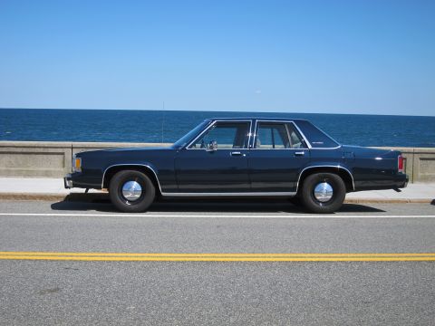 1991 Ford LTD Crown Victoria - Side view of a dark blue sedan parked by the ocean under a clear blue sky.