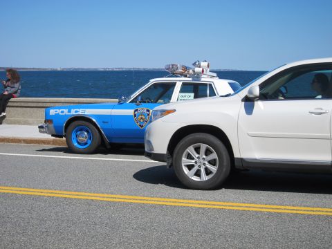 1991 Ford LTD Crown Victoria - A blue and white police car is parked next to a white SUV with the ocean in the background.