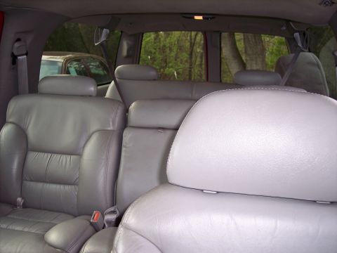 1999 Chevrolet Suburban - The interior of a vehicle shows multiple rows of gray leather seats. Another vehicle is visible outside through the rear windows.