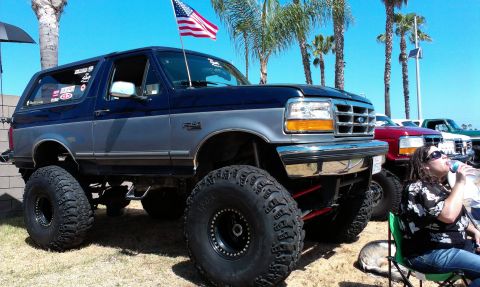 1994 Ford Bronco - This lifted 1994 Ford Bronco features a two-tone paint scheme and is parked outdoors with other vehicles and palm trees.