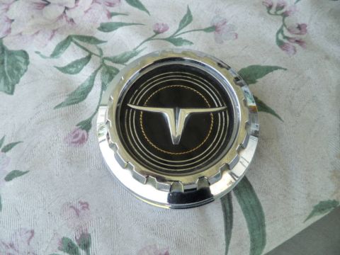 1973 Ford Ranchero - A chrome hubcap with a distinctive V-shaped emblem is shown against a floral background.