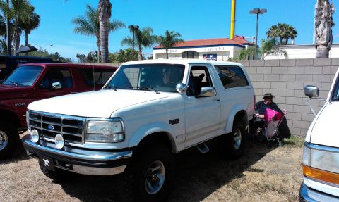 1994 Ford Bronco - A white 1994 Ford Bronco is parked next to other vehicles under a bright sky.