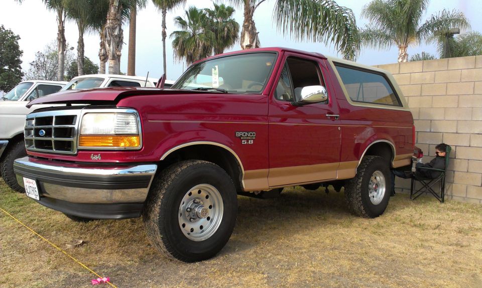 Red 1994 Ford Bronco 3/4 front view with tan trim. Another white vehicle is partially visible