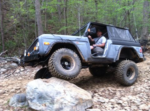 1990 Ford Bronco - A gray Ford Bronco navigates a rocky trail in a wooded area.