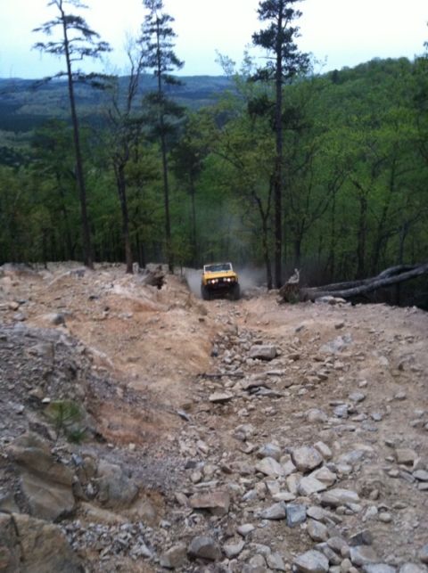 1990 Ford Bronco - A yellow off-road vehicle navigates a challenging, rocky trail surrounded by trees.