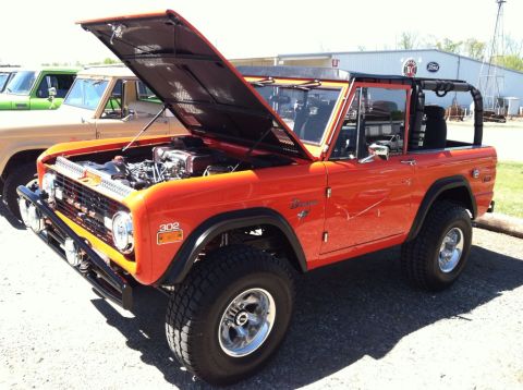 1990 Ford Bronco - Orange Ford Bronco parked in a lot with other vehicles, hood open.