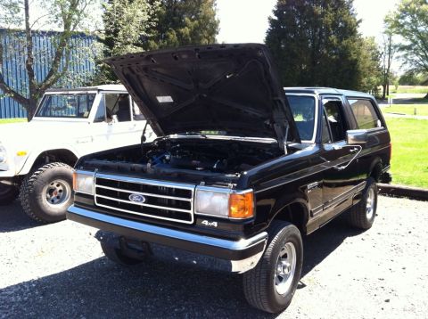 1990 Ford Bronco - A black Ford Bronco is parked outside with its hood open, next to another Bronco.