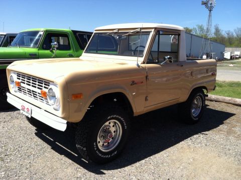 1990 Ford Bronco - A tan 1975 Ford Bronco is parked next to a green truck, with a windmill in the background.