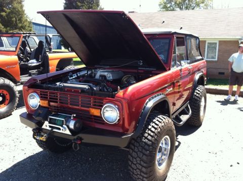 1990 Ford Bronco - A red Ford Bronco, likely from the 1970s, is parked with its hood open, revealing the engine and a winch mounted on the front bumper. Anoth…