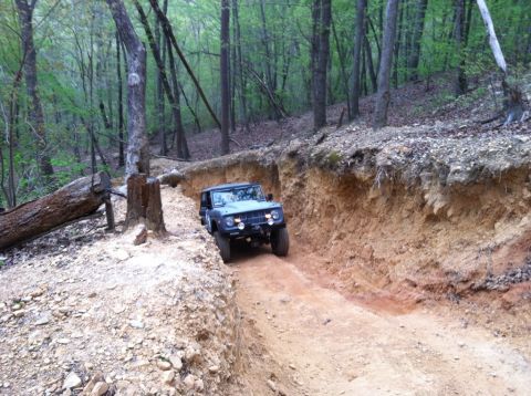 1990 Ford Bronco - A classic Ford Bronco navigates a challenging off-road trail carved into a hillside.