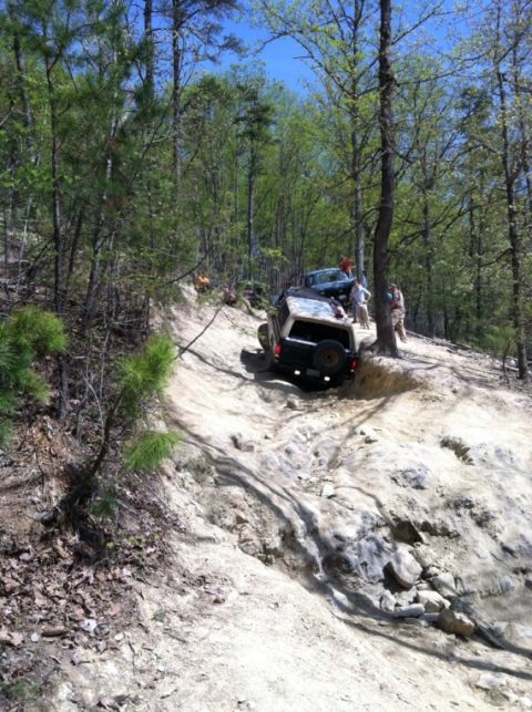 1990 Ford Bronco - Two off-road vehicles navigate a challenging dirt and rock incline in a wooded area.