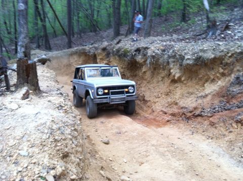 1990 Ford Bronco - A silver SUV navigates a challenging dirt trail through a wooded area.