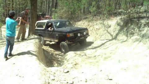 1990 Ford Bronco - Ford Bronco tackles a challenging off-road trail with spectators present.