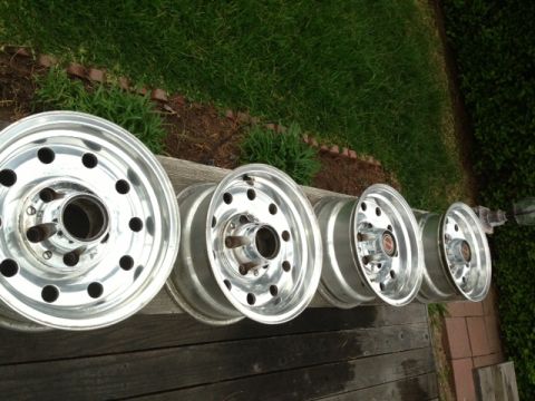1986 Ford Bronco - A set of four aluminum wheels are displayed outdoors on a wooden deck with grass in the background.