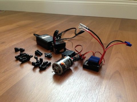 1986 Ford Bronco - RC car components including a motor, speed controller, and charger are laid out on a wooden floor.