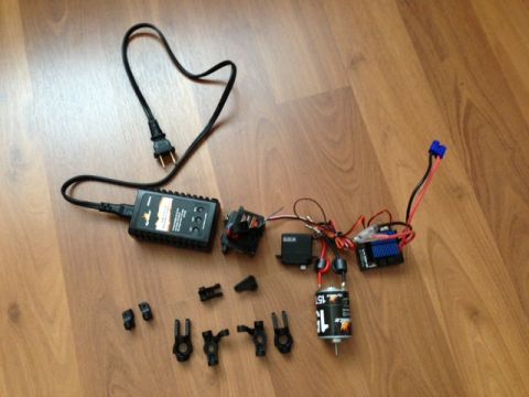 1986 Ford Bronco - Various remote control car components, including a motor, electronic speed controller, servo, and battery charger, are laid out on a wooden…