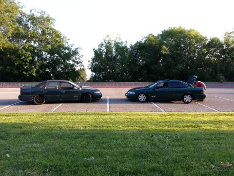 1995 Ford Taurus - Two sedans are parked in a lot, with one having its trunk open and a person partially visible inside.