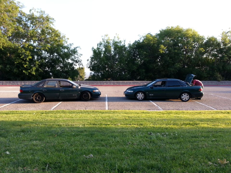 two dark green sedans parked facing each other in a lot, one with trunk open