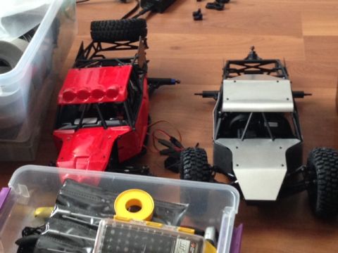 1986 Ford Bronco - Two remote-controlled off-road vehicles are shown, one red and one silver, with various parts and tools scattered around them.