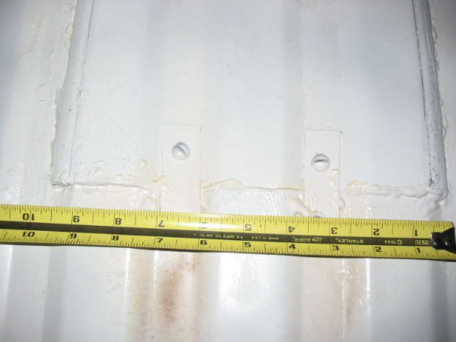 Tape measure laid across a white metal panel with two welded tab brackets