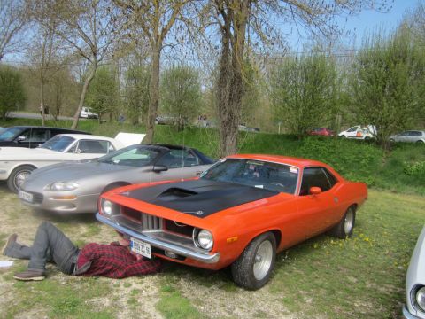1991 Ford LTD Crown Victoria - A person works on an orange muscle car parked next to a silver sports car on a grassy lot.