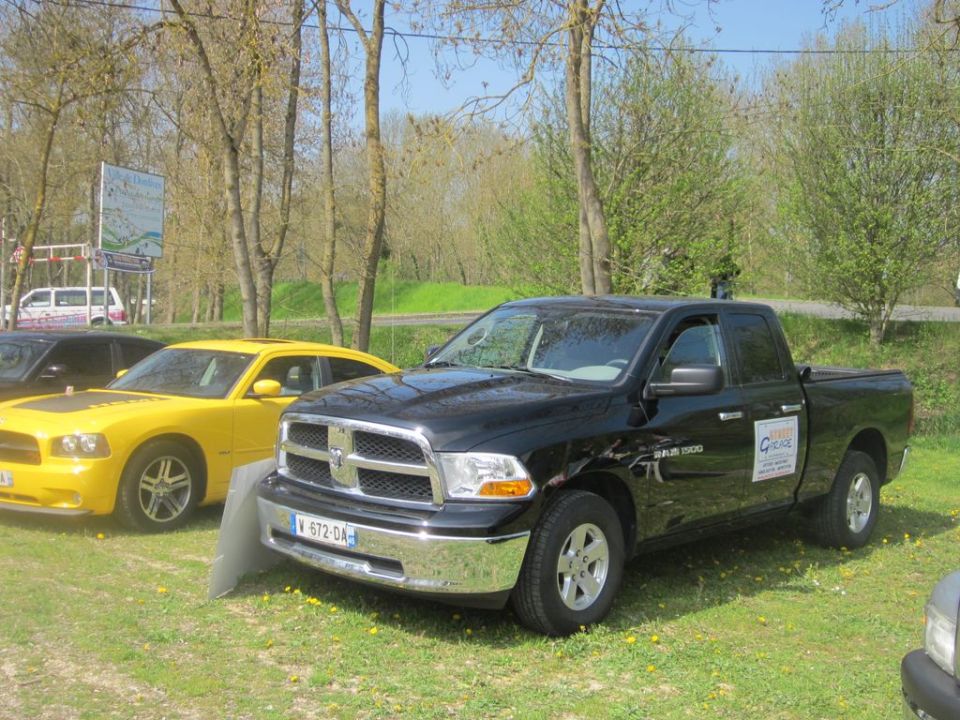 Black Dodge Ram 1500 pickup truck parked on grass, front 3/4 view. Yellow car to the left