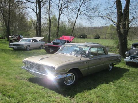1991 Ford LTD Crown Victoria - A gold 1959 Buick LeSabre coupe is parked on a grassy field, with several other vehicles visible in the background.