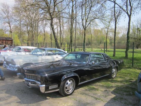 1991 Ford LTD Crown Victoria - Two classic cars, a black Cadillac Eldorado and a lighter one, parked outdoors under trees.