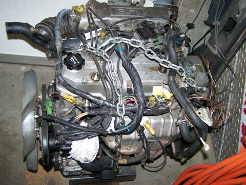 1988 Suzuki Samurai - This engine assembly features a fan, various hoses, and electrical wiring, with chains secured for handling.