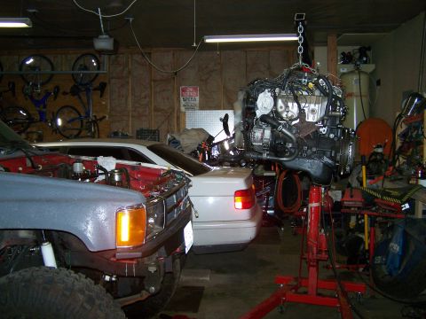 1988 Suzuki Samurai - An engine is hoisted for work in a garage, with a truck and a sedan visible in the background.