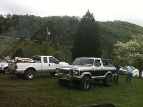 1992 Ford Bronco - A two-tone silver and black Ford Bronco is parked on a grassy field with a white pickup truck nearby.