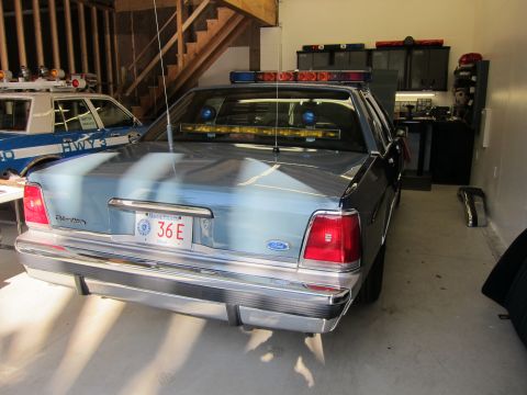 1991 Ford LTD Crown Victoria - A light blue 1991 Ford Crown Victoria LTD police car is parked in a garage next to another police vehicle.