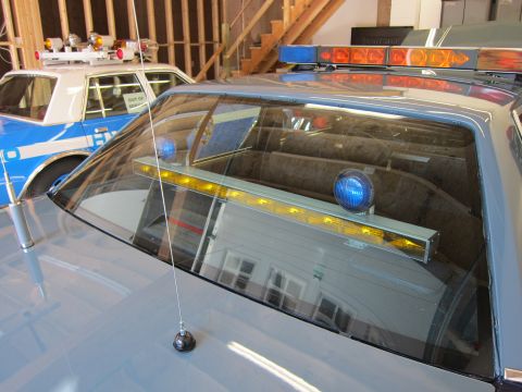 1991 Ford LTD Crown Victoria - Close-up of the interior light bar and rear window of a police car, with another police vehicle in the background.