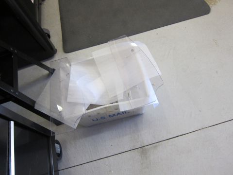 1991 Ford LTD Crown Victoria - Clear plastic sheets are stacked inside a U.S. Mail bin on a concrete floor.