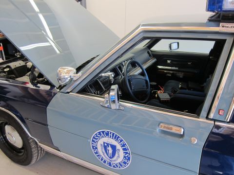 1991 Ford LTD Crown Victoria - The interior of a 1991 Ford Crown Victoria LTD police car is visible with the hood open, showing the Massachusetts State Police emblem on t…